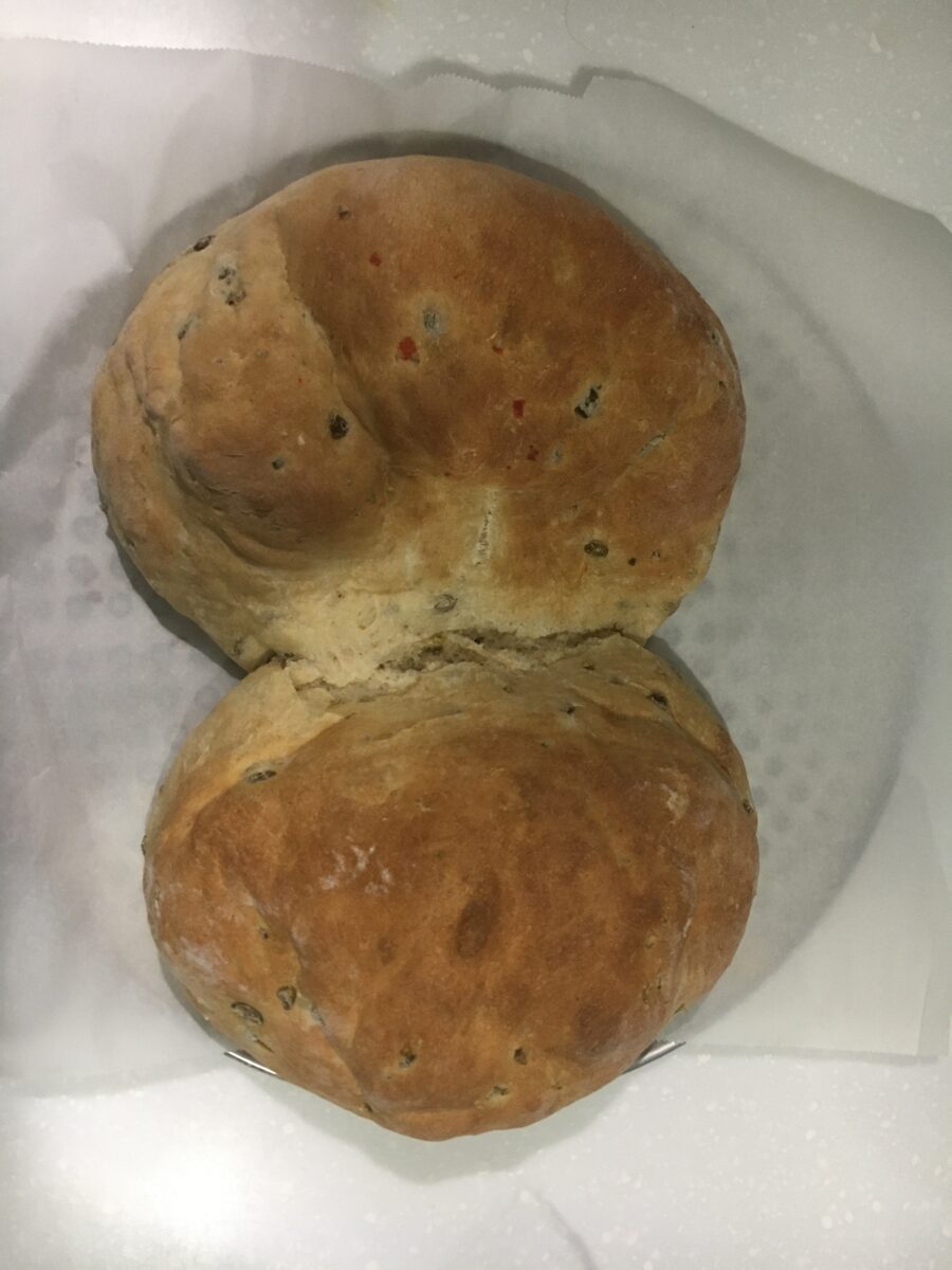 Medium-sized pizza tray with parchment paper on which sit two small loaves of olive bread.