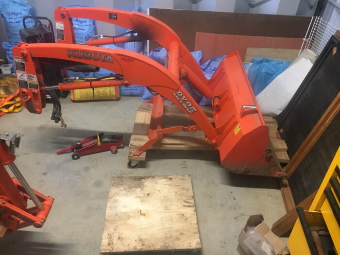 The front-loader sitting on its dolly in the corner of the steel shed, with the snowblower dolly in front of it